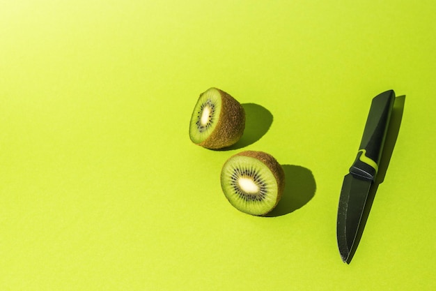 Un cuchillo y una fruta cortada de un kiwi maduro sobre un fondo verde.