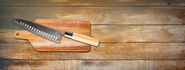 Cuchillo de jefe gyuto japonés tradicional sobre una tabla de cortar. Bandera de fondo de madera vieja