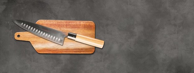 Cuchillo de jefe gyuto japonés tradicional sobre una tabla de cortar. Banner de fondo de hormigón