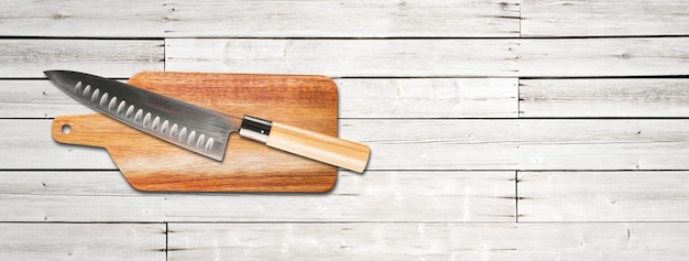 Cuchillo de jefe gyuto japonés tradicional sobre una tabla de cortar. Banner de fondo de madera blanca