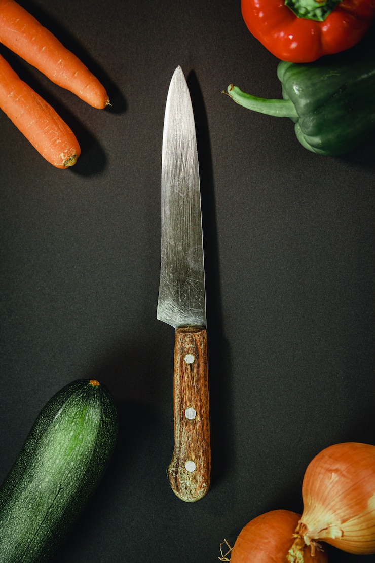 Foto cuchillo largo rodeado de diferentes verduras.
