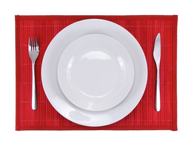 Cuchillo de mesa, plato, tenedor sobre fondo de color rojo.