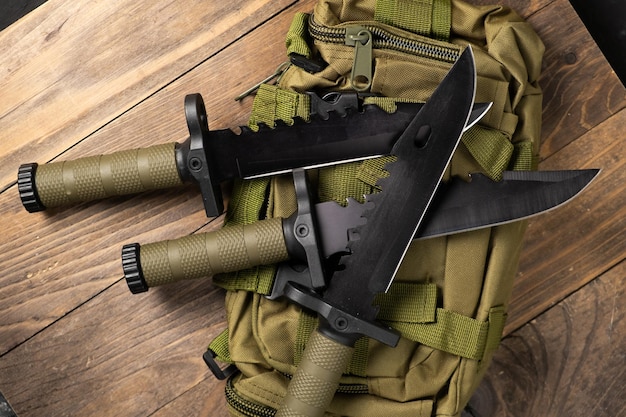 Un cuchillo militar moderno y una funda de plástico para él Las armas afiladas yacen en una mochila militar de color oliva