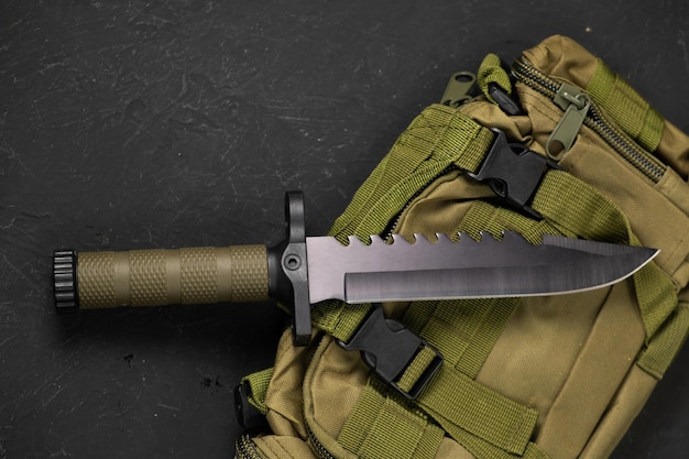 Un cuchillo militar moderno y una funda de plástico para él Las armas afiladas yacen en una mochila militar de color oliva