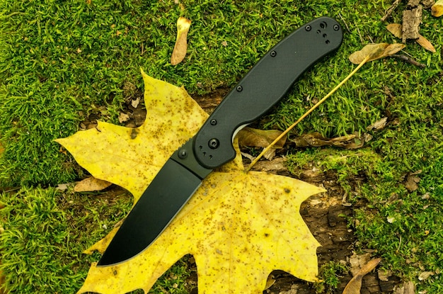 Cuchillo plegable negro en la hoja de otoño en el bosque con un cuchillo vista superior