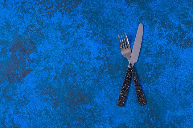 Foto cuchillo y tenedor de mesa sobre un fondo azul.