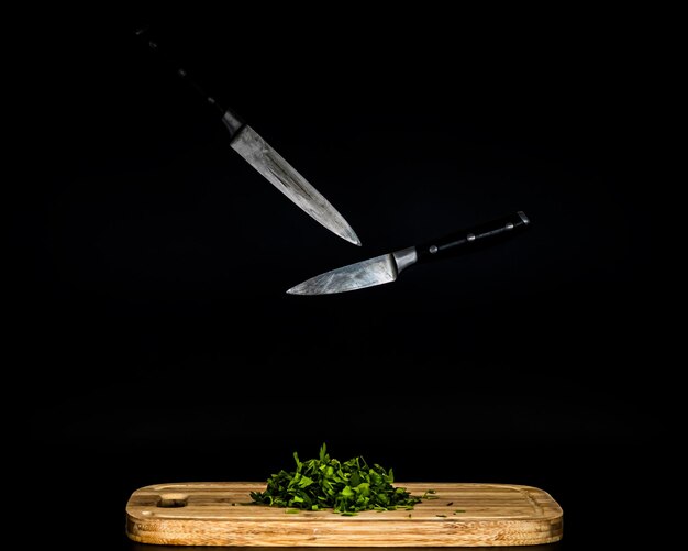 Foto cuchillos colgando en el aire y perejil picado verde en la tabla de cortar comida de fondo negro