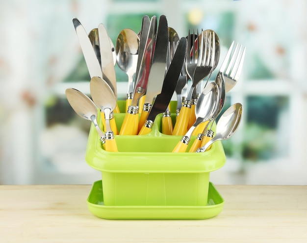 Foto cuchillos cucharas tenedores en recipiente de plástico para secar sobre fondo brillante
