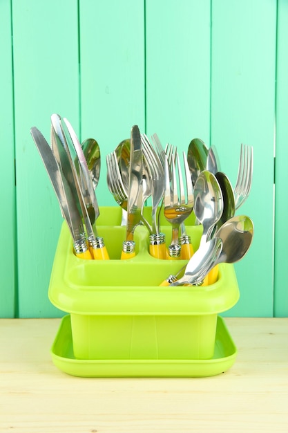 Foto cuchillos cucharas tenedores en recipiente de plástico para secar sobre fondo de madera de color