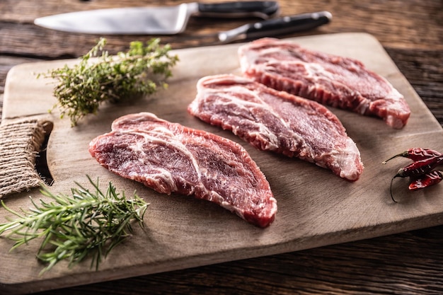 Cuello de cerdo crudo cortado en una tabla de cortar con hierbas de romero y tomillo