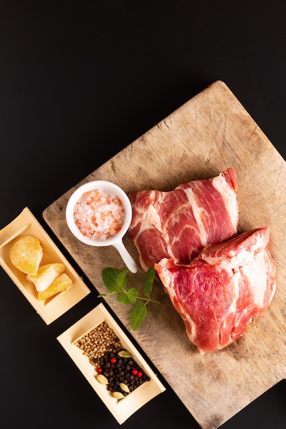 Cuello de cerdo deshuesado del pedazo del concepto de la comida en la tabla de cortar con la especia en fondo negro con el espacio de la copia