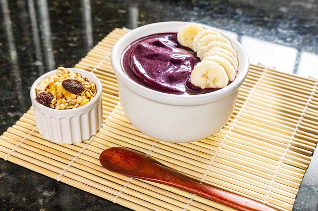 Cuenco de Acai con plátano y cereal en mantel de bambú.