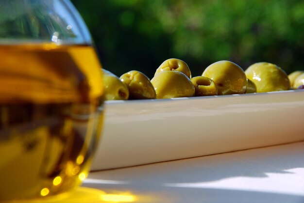 Foto un cuenco de aceitunas con un vaso de aceite de oliva al fondo.