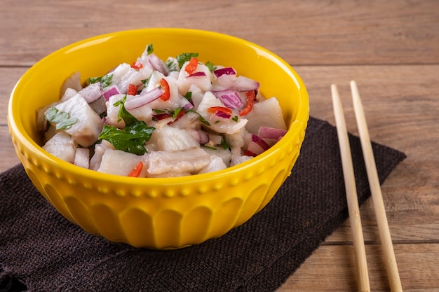 Un cuenco amarillo con ceviche sobre una mesa de madera.