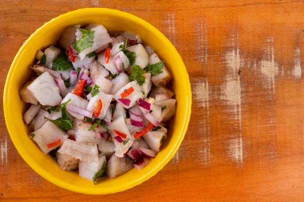 Un cuenco amarillo con ceviche sobre una mesa de madera.