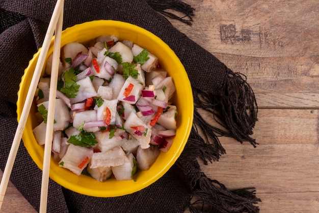 Un cuenco amarillo con ceviche sobre una mesa de madera.