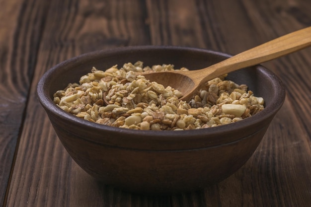 Un cuenco de arcilla con granola y una cuchara de madera sobre una mesa de madera