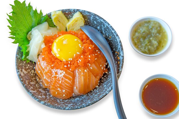 Cuenco de arroz japonés con sashimi de salmón en rodajas, huevos pasados por agua, huevas de camarón con salsa de mariscos, enfoque selectivo