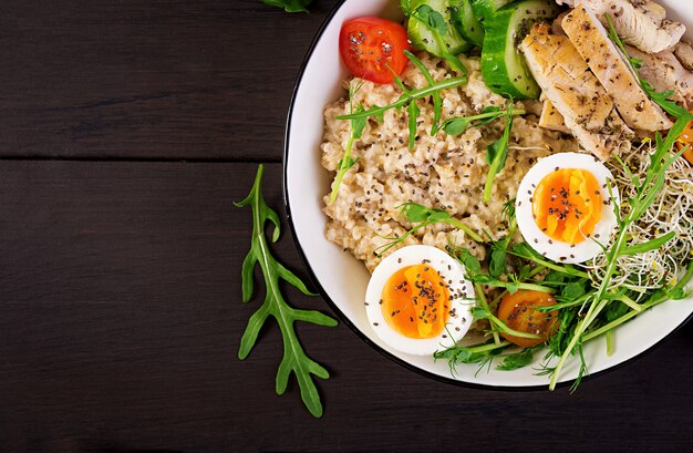 Cuenco con avena, filete de pollo, tomate, lechuga, microgreens y huevo cocido