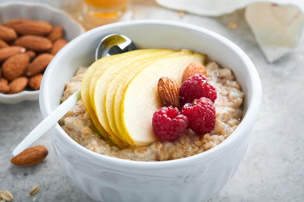 Cuenco de avena con pera de frambuesa y miel sobre fondo de mesa antigua de hormigón gris Comida caliente y saludable para el desayuno vista superior plana