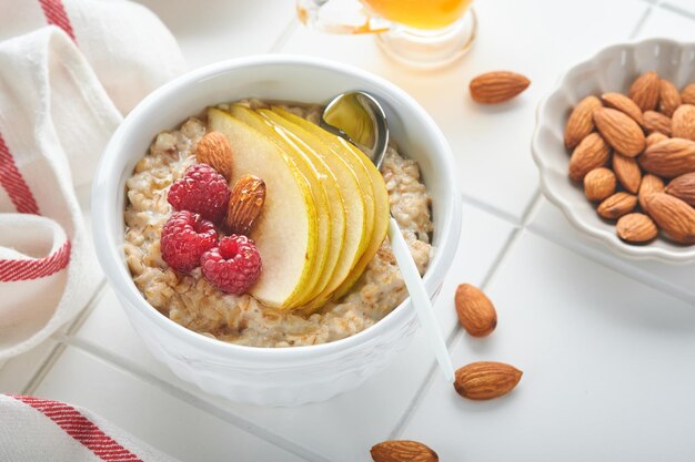 Cuenco de avena con pera de frambuesa y miel sobre fondo de mesa antigua de hormigón gris Comida caliente y saludable para el desayuno vista superior plana