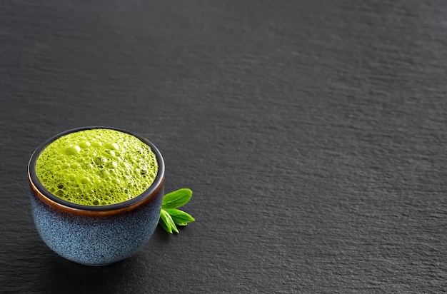 Cuenco de azul con té verde matcha, junto a hojas de té