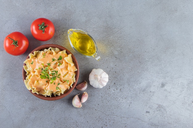 Cuenco de barro de deliciosos macarrones cremosos con aceite y verduras sobre fondo de piedra.