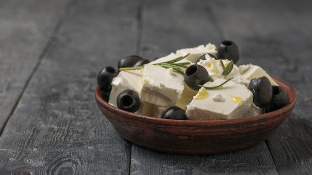 Un cuenco de barro con rodajas de queso feta, aceitunas y aceite de oliva sobre una mesa de madera. Queso natural elaborado con leche de oveja.