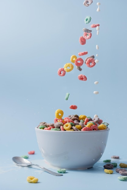 Foto cuenco blanco con coloridos cereales en forma de anillo y leche cereales y leche vertiendo en el cuenco