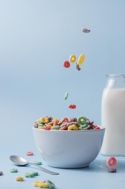 Foto cuenco blanco con coloridos cereales en forma de anillo y leche cereales y leche vertiendo en el cuenco