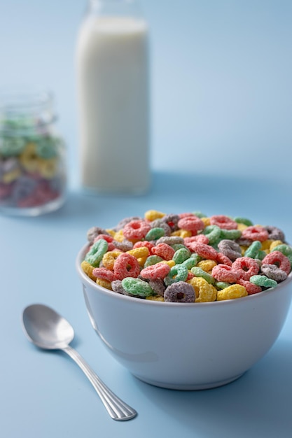 Cuenco blanco con coloridos cereales en forma de anillo y leche sobre un fondo azul