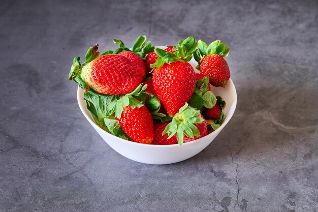 Un cuenco blanco con fresas sobre un fondo de pizarra negra