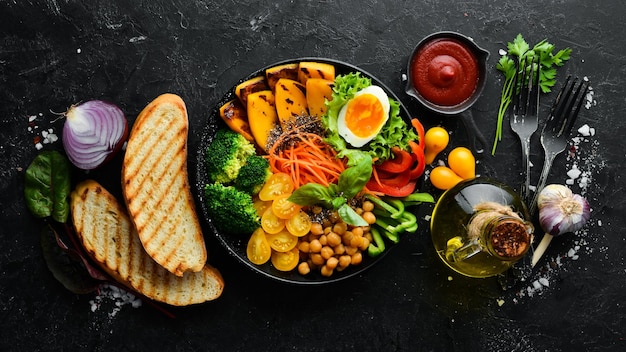 Cuenco de Buda calabaza brócoli huevo tomates zanahorias pimentón en un plato negro sobre un fondo negro Vista superior Espacio libre para el texto