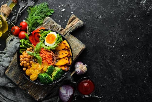 Cuenco de Buda calabaza brócoli huevo tomates zanahorias pimentón en un plato negro sobre un fondo negro Vista superior Espacio libre para el texto