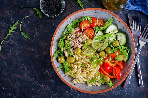 Cuenco de buda Ensalada de pasta con atún, tomates, aceitunas, pepino, pimiento dulce y rúcula sobre fondo rústico