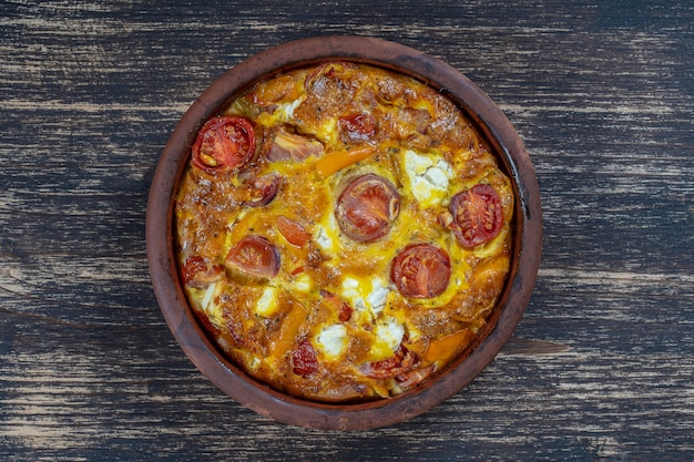 Cuenco de cerámica con frittata de verduras, comida vegetariana sencilla. Frittata con tomate, pimiento, cebolla y queso feta en la mesa de madera, de cerca. Tortilla de huevo italiana, vista superior