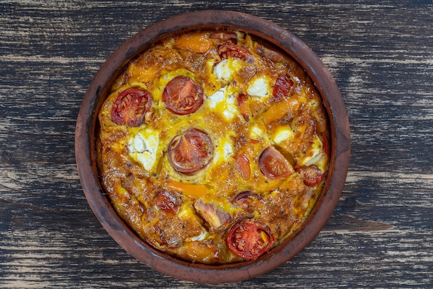 Cuenco de cerámica con frittata de verduras, comida vegetariana sencilla. Frittata con tomate, pimiento, cebolla y queso feta en la mesa de madera, de cerca. Tortilla de huevo italiana, vista superior