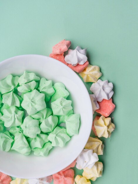 Cuenco de cerámica lleno de merengues coloridos con fondo de menta pastel