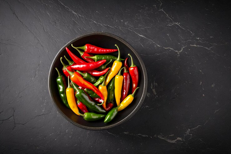 Un cuenco de chiles mezclados de varios tamaños y colores colocados en una superficie de piedra oscura