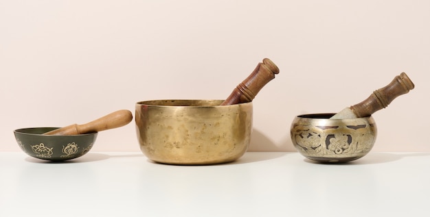 Foto cuenco de cobre y badajo de madera sobre una mesa blanca. instrumento musical para meditación, relajación, diversas prácticas médicas relacionadas con los biorritmos, normalización de la salud mental.