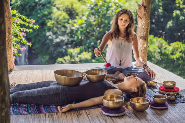 Foto cuenco de cobre de buda de nepal en el salón de spa hermosa mujer joven haciendo terapia de masaje cantando