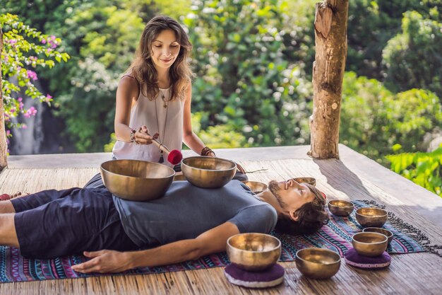 Cuenco de cobre de Buda de Nepal en el salón de spa joven hombre hermoso haciendo terapia de masaje cantando