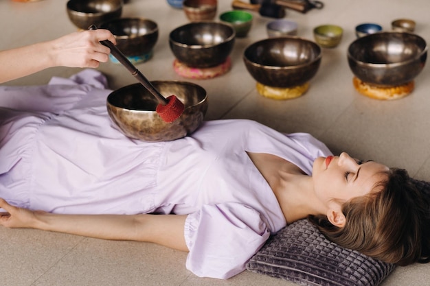 El cuenco de cobre del Buda nepalí en el spa Una mujer hermosa joven está haciendo un masaje con cuencos de canto en un salón de spa con el telón de fondo de una cascada