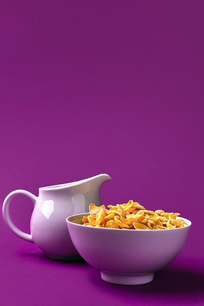Foto cuenco con copos de maíz jarra de leche sobre fondo morado concepto de un desayuno saludable