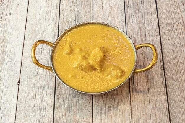 Cuenco con curry amarillo korma de pollo suave con salsa de yogur y leche de coco sobre mesa blanca