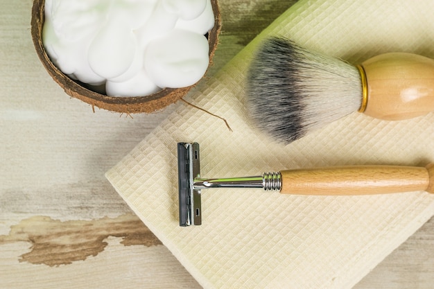 Un cuenco de espuma de afeitar, un cepillo y una navaja sobre una toalla sobre una mesa de madera. Accesorios masculinos para el cuidado de la apariencia. Endecha plana.