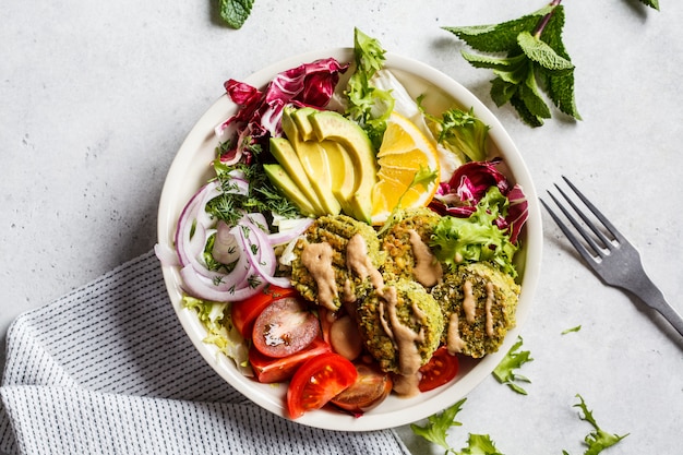 Cuenco de falafel al horno con ensalada de verduras, aderezo de tahini y aguacate, vista superior.