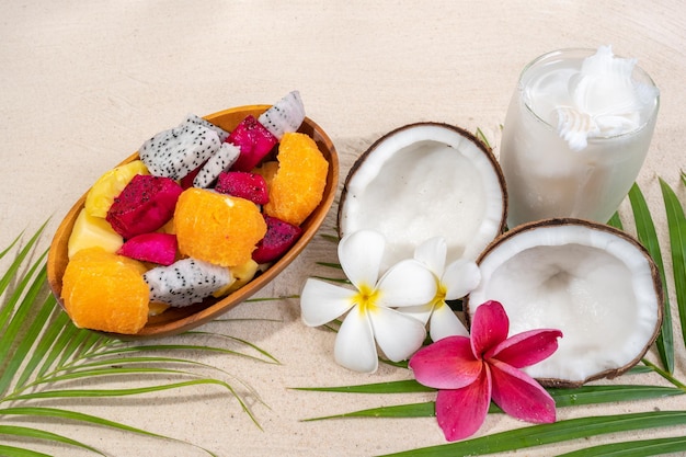 Cuenco de frutas mixtas y jugo de coco en hoja de palma en la playa de arena.