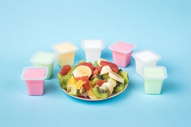 Un cuenco con frutas en rodajas y tazas con yogur multicolor sobre un fondo azul. Alimentos con leche y frutas.