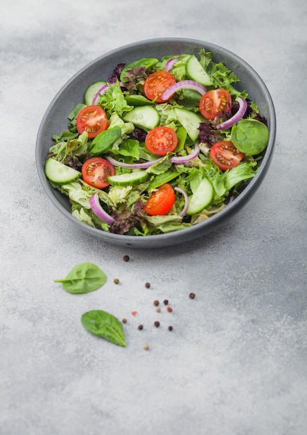 Cuenco gris en movimiento con ensalada saludable de verduras frescas con lechuga y tomates, cebolla roja y espinacas sobre fondo claro El mejor concepto de comida vegetariana